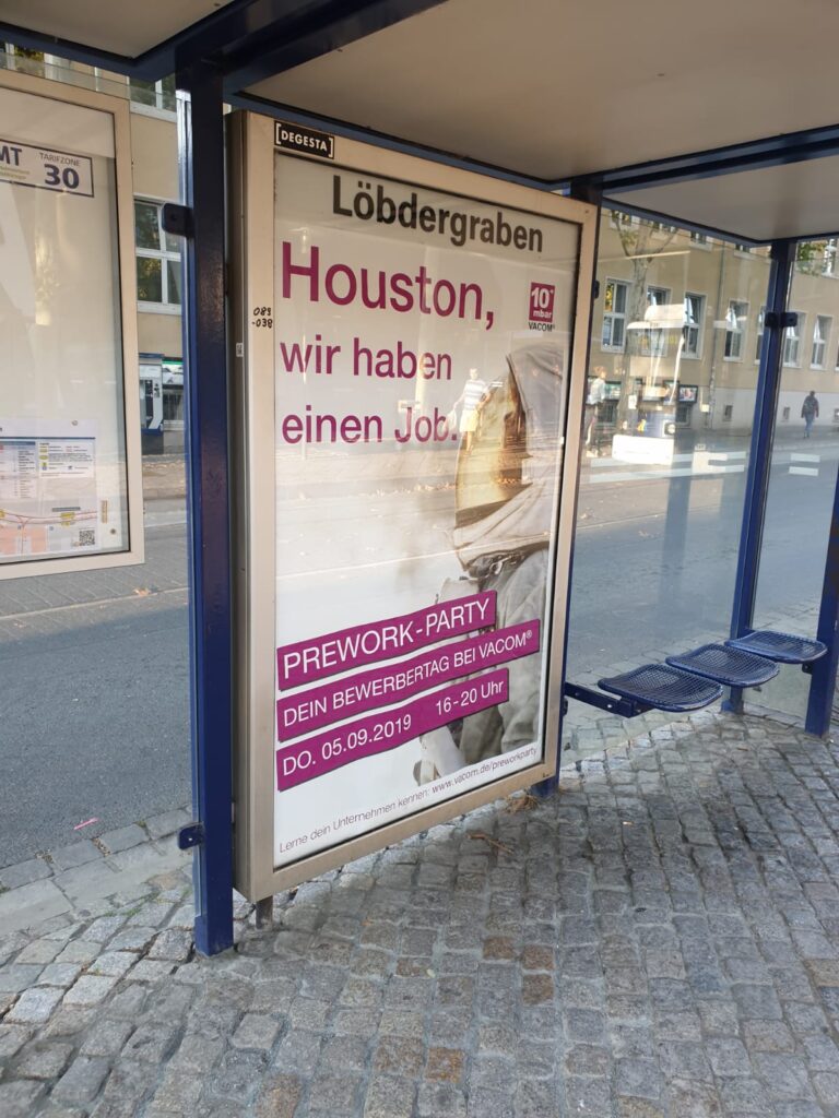 A foto from a bus stop and a poster. The poster advertises a prework-party in the year 2019 for the company VACOM