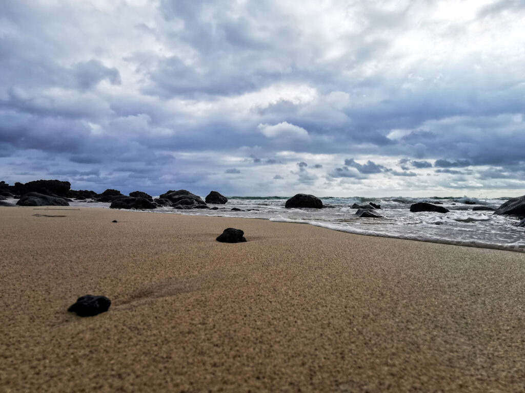A photography of a cloudy beach on Fuerteventura, there a black rocks spreaded over the sand.